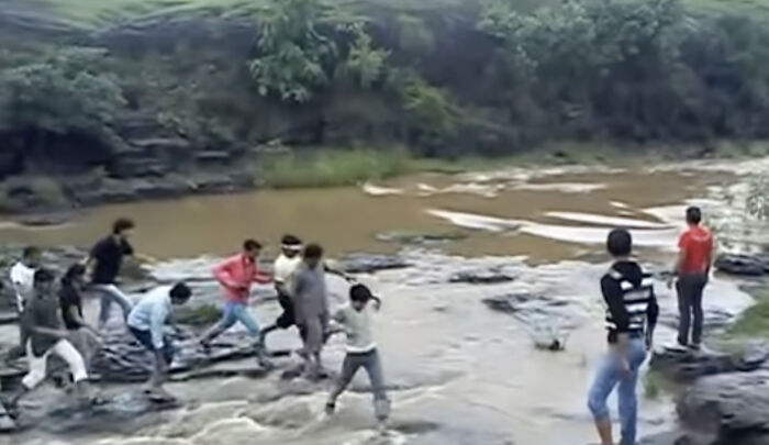 Grupo de personas cruzando un río con agua turbulenta en un entorno natural, capturado en grabación inquietante.