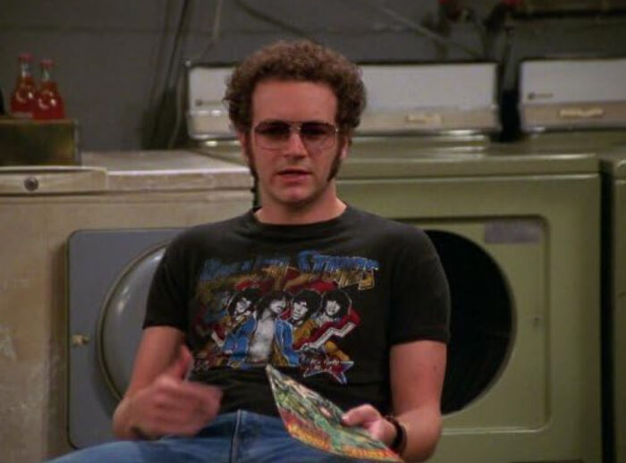 Man wearing sunglasses and a retro band t-shirt sitting in a laundry room, capturing disappointment in someone idolized.