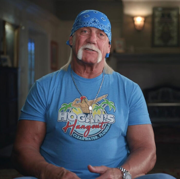 Man with blue bandana and vintage Hogan's Hangout t-shirt in casual indoor setting, reflecting disappointment in idolized figure.
