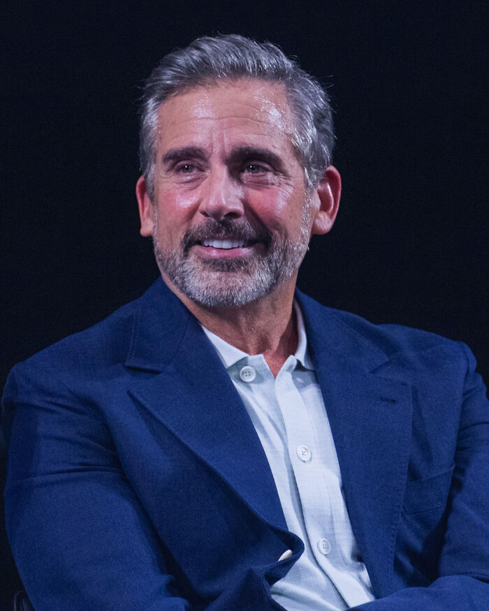 Middle-aged Hollywood star with gray hair and beard, wearing a blue blazer and white shirt, representing fame after 30.
