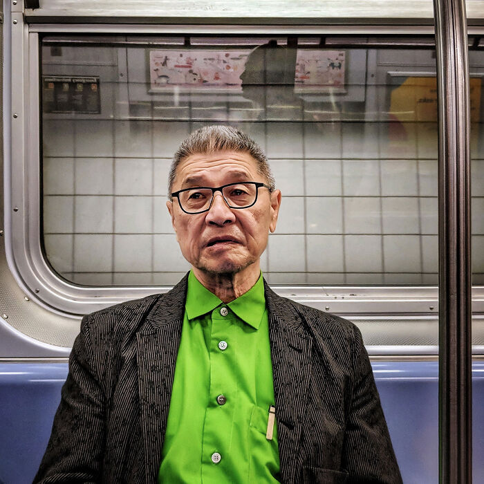 Elderly man in glasses and green shirt captured in a street portrait inside NYC subway train, showcasing life underground.