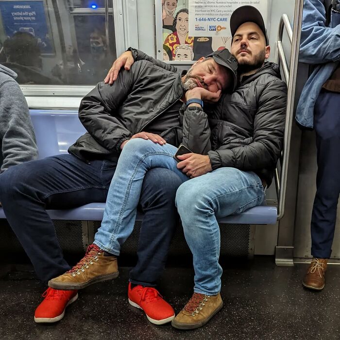 Two men wearing jackets and jeans resting closely together on a New York City subway, showcasing life underground street portraits.