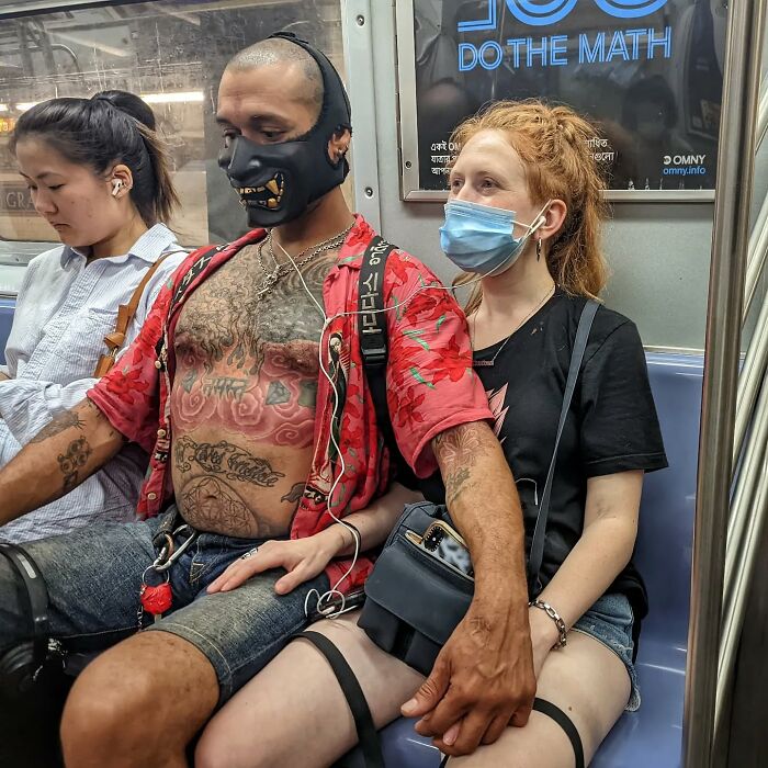 Man with tattoos and unique face mask holding hands with woman wearing a mask in a candid NYC subway street portrait.