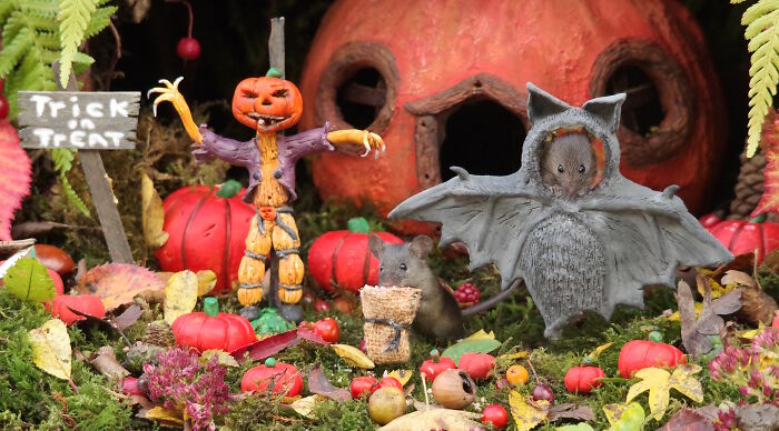 Halloween village setup in garden with wild mice dressed in costumes among mini pumpkins and decorations.
