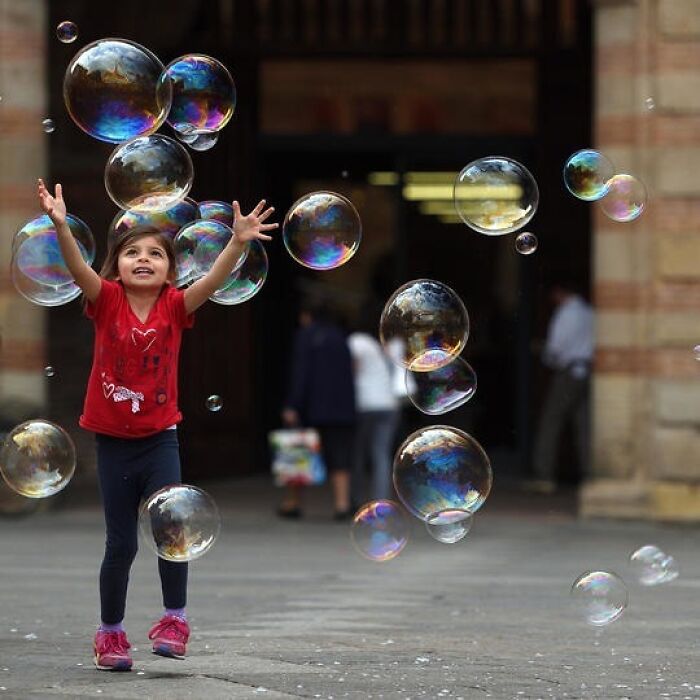 Young girl joyfully playing with bubbles outdoors, capturing beautiful photos of childhood around the world.