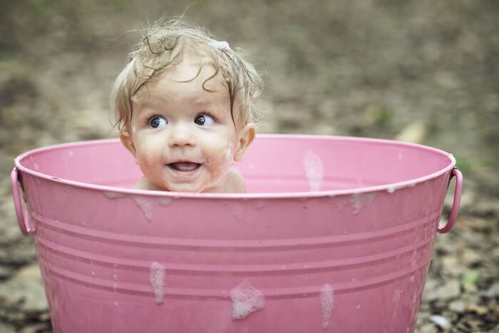 Happy baby with wet hair playing in a pink bucket outdoors, capturing a beautiful moment of childhood around the world.