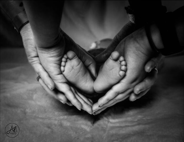 Black and white photo of adult hands gently holding a baby’s feet, symbolizing childhood and care around the world.