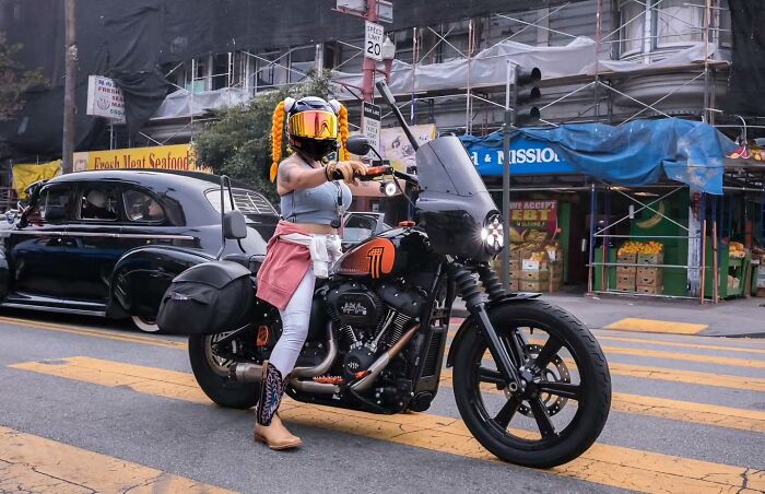 Street photographer captures humor and chaos of everyday life with a woman on a motorcycle in an urban street setting.