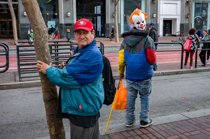 Street photographer captures humor and chaos in everyday life with a man in a clown mask and a man holding a tree on the street.