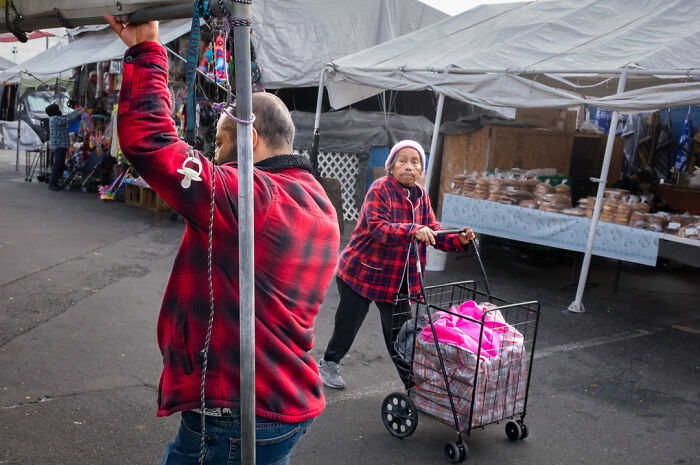 Man and woman in red plaid jackets at an outdoor market, capturing humor and chaos in everyday street photography.