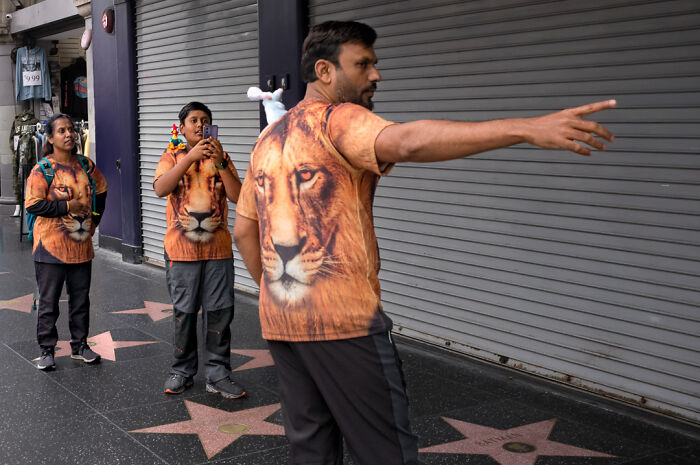 Three people wearing matching lion print shirts on a city sidewalk, capturing everyday humor and chaos in street photography.