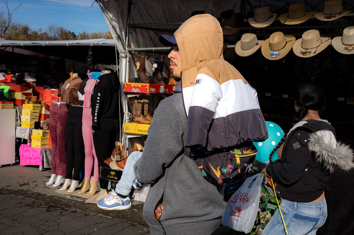 Street photographer captures humor and chaos of everyday life at a busy outdoor market with shoppers and colorful displays.