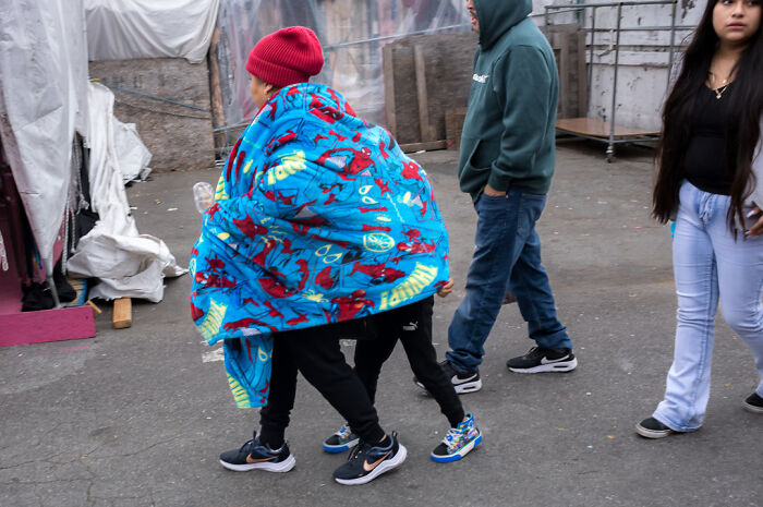 Street photographer captures humor and chaos in everyday life with people walking, wrapped in a colorful blanket on a city street.
