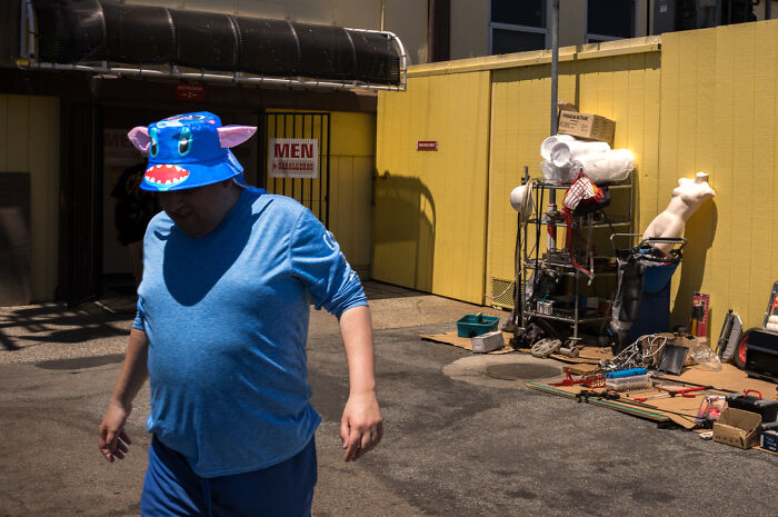 Man wearing a colorful monster bucket hat walking past chaotic street scene captured by street photographer