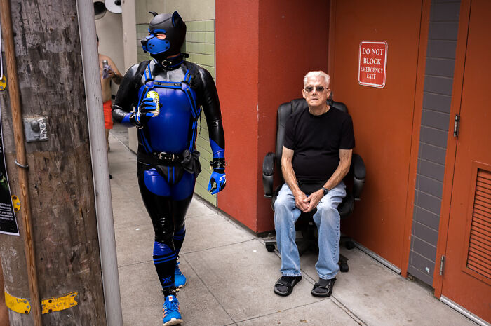 Street photographer captures humor and chaos with a man in a blue costume walking past an elderly man sitting outside.
