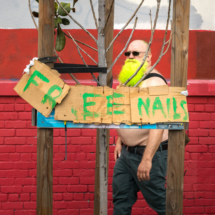 Street photographer captures humor and chaos in everyday life, featuring a man with a bright yellow beard by a handmade sign.