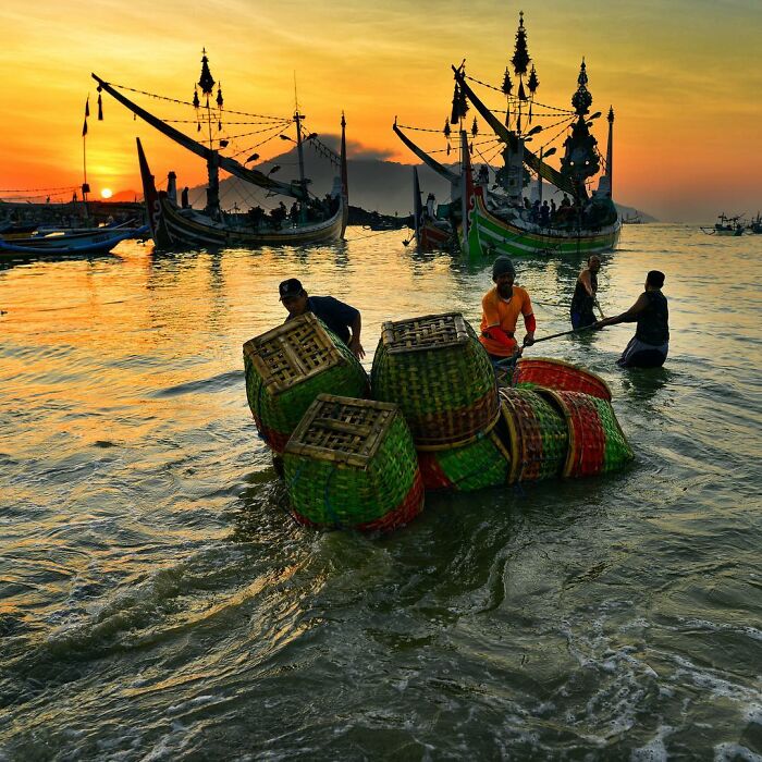 Fishermen unloading baskets in the water at sunrise, showcasing candid photos capturing life’s beauty through Harjanto Sumawan’s lens.