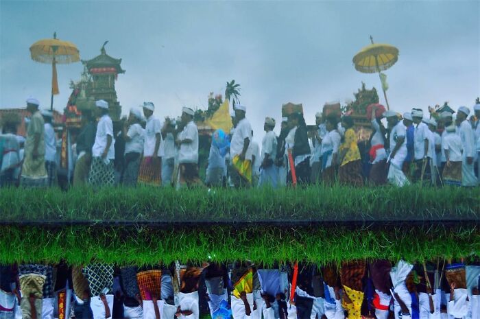 Candid photo of a traditional procession with vibrant clothing and umbrellas captured through Harjanto Sumawan’s lens.