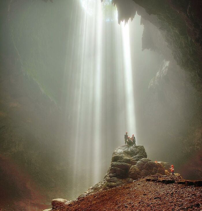 People exploring a cave illuminated by sunbeams through Harjanto Sumawan’s lens capturing life’s beauty in nature.
