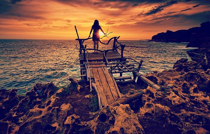 Silhouette of a person standing on a wooden pier at sunset, capturing life’s beauty through Harjanto Sumawan’s lens.