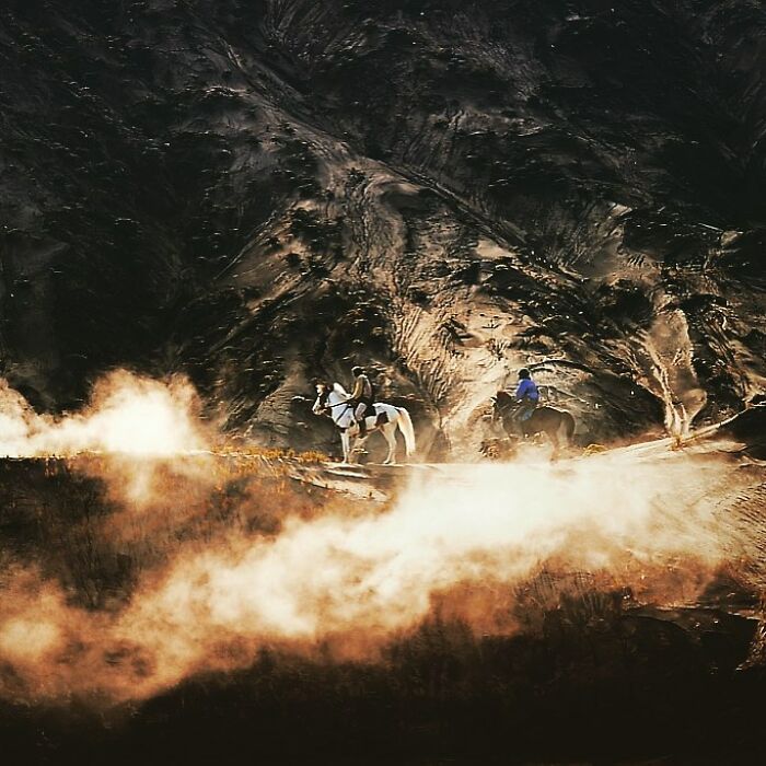 Two people riding horses along a misty trail with rugged mountains in the background, candid photo capturing life’s beauty.