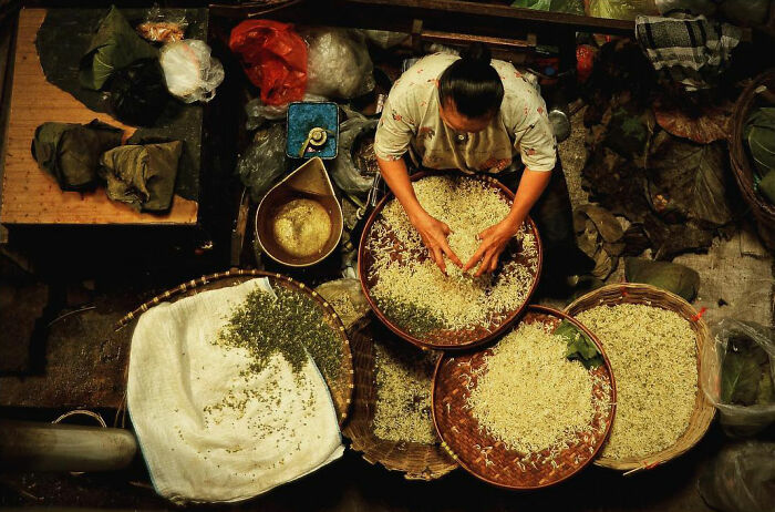 Woman sorting grains by hand in baskets, showcasing candid photos capturing life’s beauty through Harjanto Sumawan’s lens.