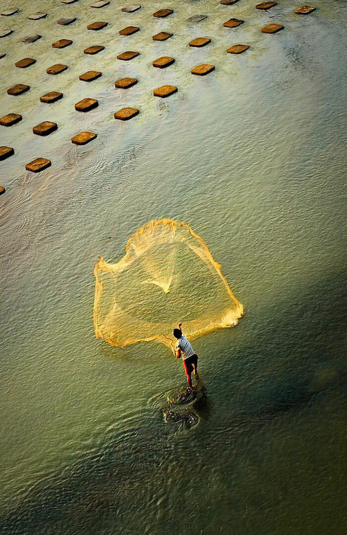 Fisherman casting a net in shallow water, captured candidly through Harjanto Sumawan’s lens showcasing life’s beauty.