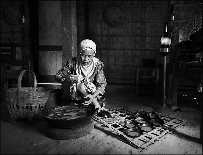 Elderly woman preparing traditional food in a rustic setting, captured through Harjanto Sumawan’s candid photography style.