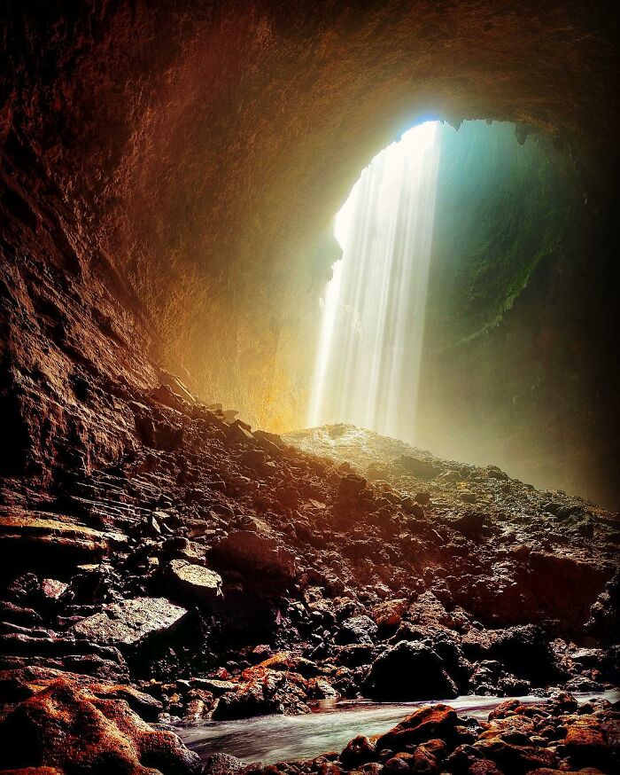 Sunlight streaming through cave entrance illuminating rugged rocky terrain, showcasing life’s beauty in candid photography.