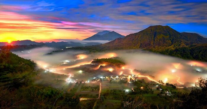 Sunrise over misty valley with glowing village lights and mountains, showcasing candid photos capturing life’s beauty.