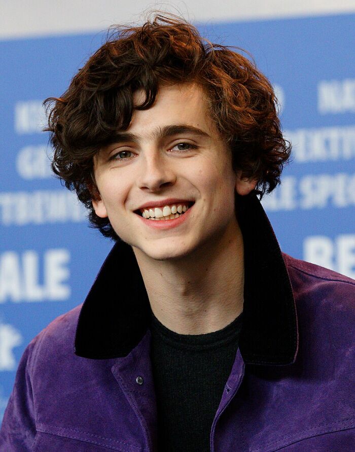 Young male celeb smiling with curly hair and wearing a purple jacket, featured in people sharing celebs they can't stand.