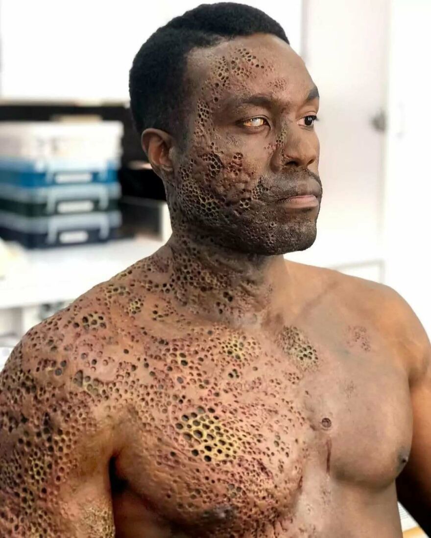 Man with trypophobia-inspired makeup showing clusters of tiny holes on his face and upper body in a studio setting.