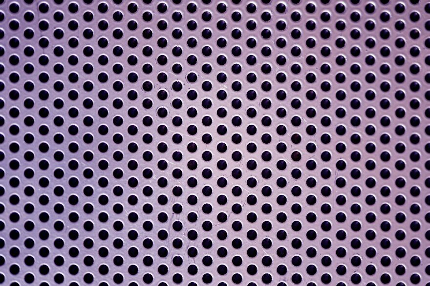 Close-up of purple surface with evenly spaced tiny holes illustrating trypophobia brain reaction concept.