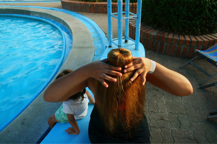 Person with long hair styled in a bun near pool, showing a captivating and witty street coincidence captured by Tavepong Pratoomwong.