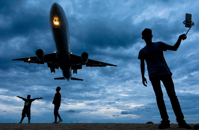 Silhouettes capturing a street coincidence with a low-flying airplane against a dramatic cloudy sky.