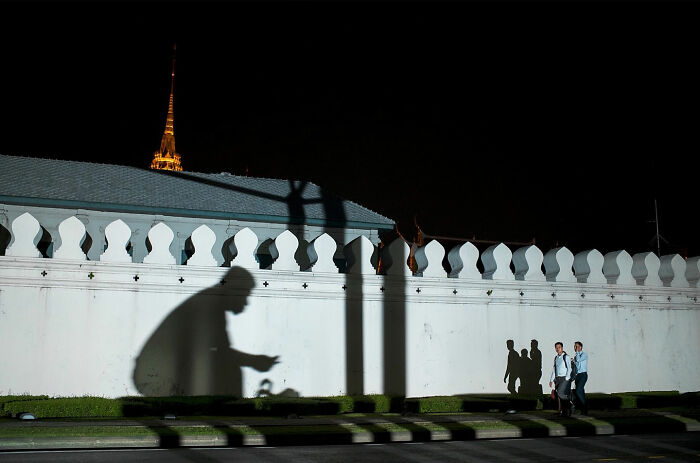 Large shadow of a cyclist on a white wall at night alongside people walking, illustrating captivating street coincidences.