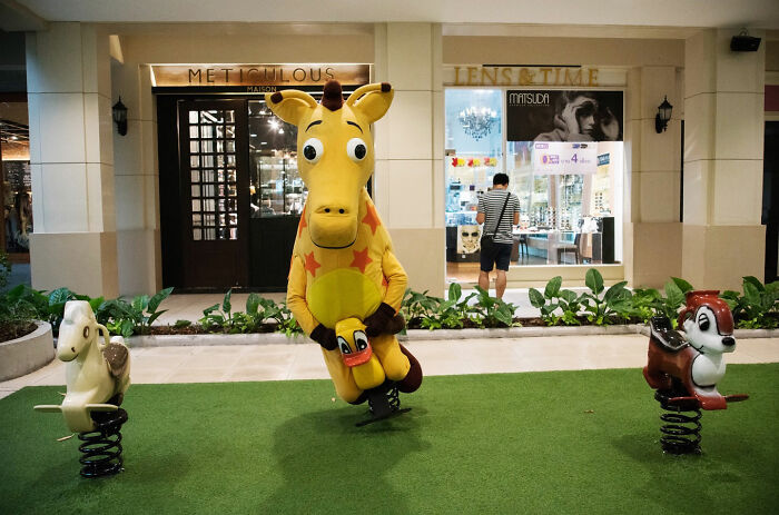 Person in giraffe costume on spring rider in outdoor urban play area, capturing funny street coincidences.