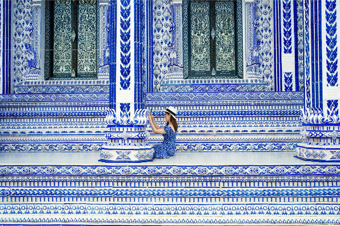 Woman in a matching blue dress and hat sitting against a detailed blue and white patterned wall showcasing street coincidences.
