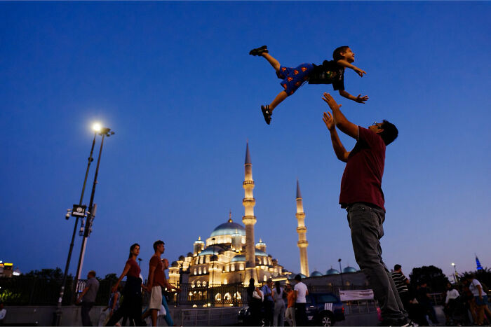 Child playfully thrown in the air by adult near illuminated mosque at dusk, showcasing captivating street coincidences.