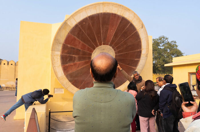 Man photographing large circular structure while others observe, showcasing captivating street coincidences in a public setting.
