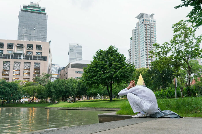 Person wearing white with a yellow cone hat sitting by a pond in an urban park, illustrating street coincidences.