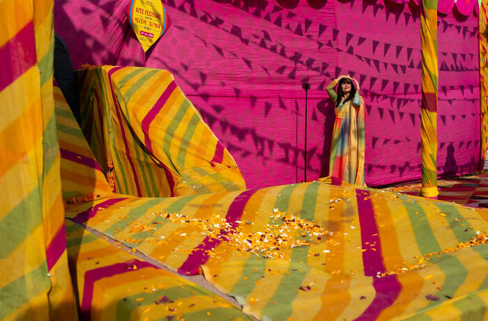 Woman in multicolored dress standing against vibrant striped and patterned fabric backdrop in street coincidence scene