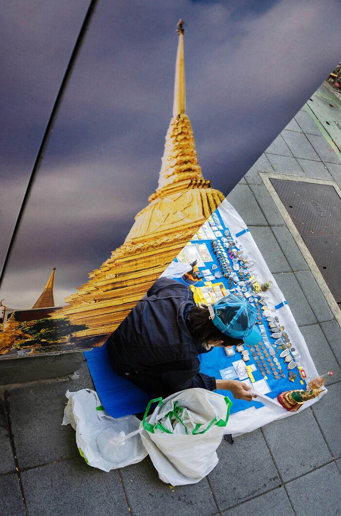 Street coincidences featuring a vendor arranging souvenirs beside a giant temple image on a city sidewalk.