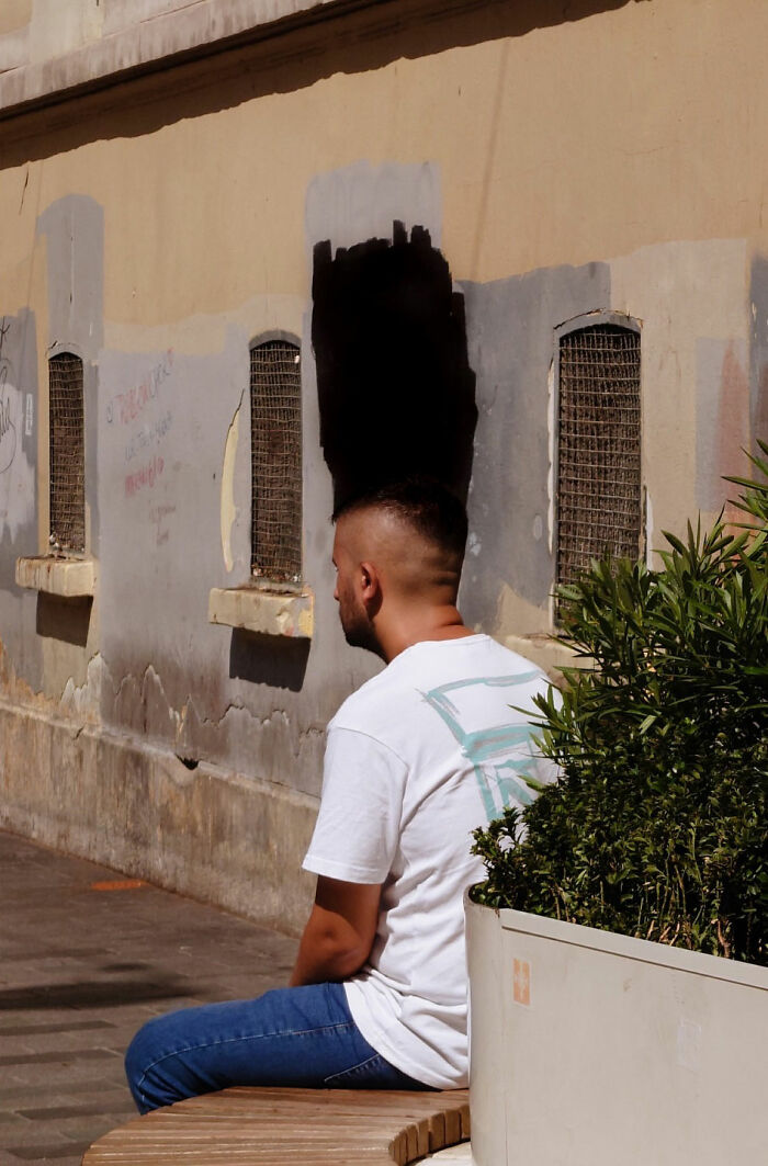 Man sitting on bench with shadow blending into wall painted with street coincidences captured by Tavepong Pratoomwong