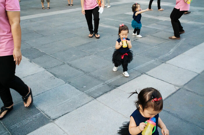 Several toddlers dressed alike walking and drinking from bottles on a paved street showcasing street coincidences.