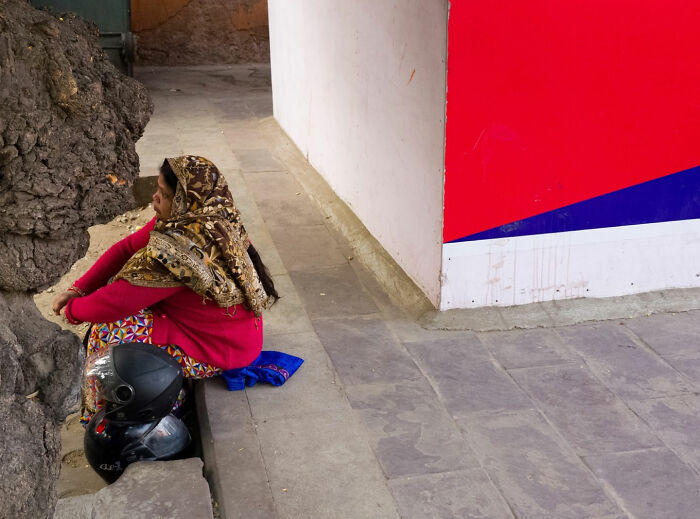 Woman sitting beside a tree on a sidewalk showing a street coincidence captured by Tavepong Pratoomwong.