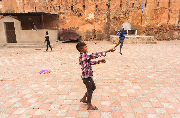 Children playing and flying kites in a courtyard, capturing a charming street coincidence moment by Tavepong Pratoomwong.