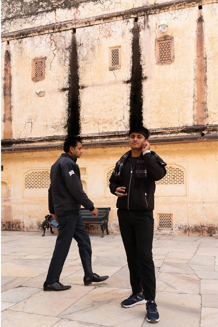 Two men in black jackets standing and walking near a weathered wall, illustrating street coincidences captured by Tavepong Pratoomwong.