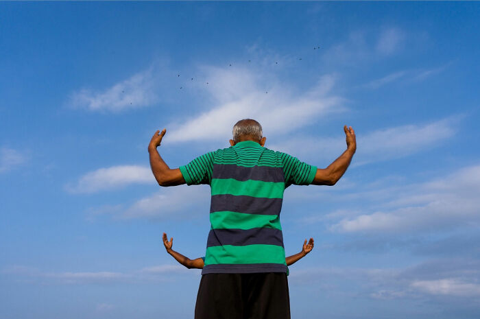 Man in green striped shirt with arms raised against the sky, showcasing a captivating street coincidence moment.