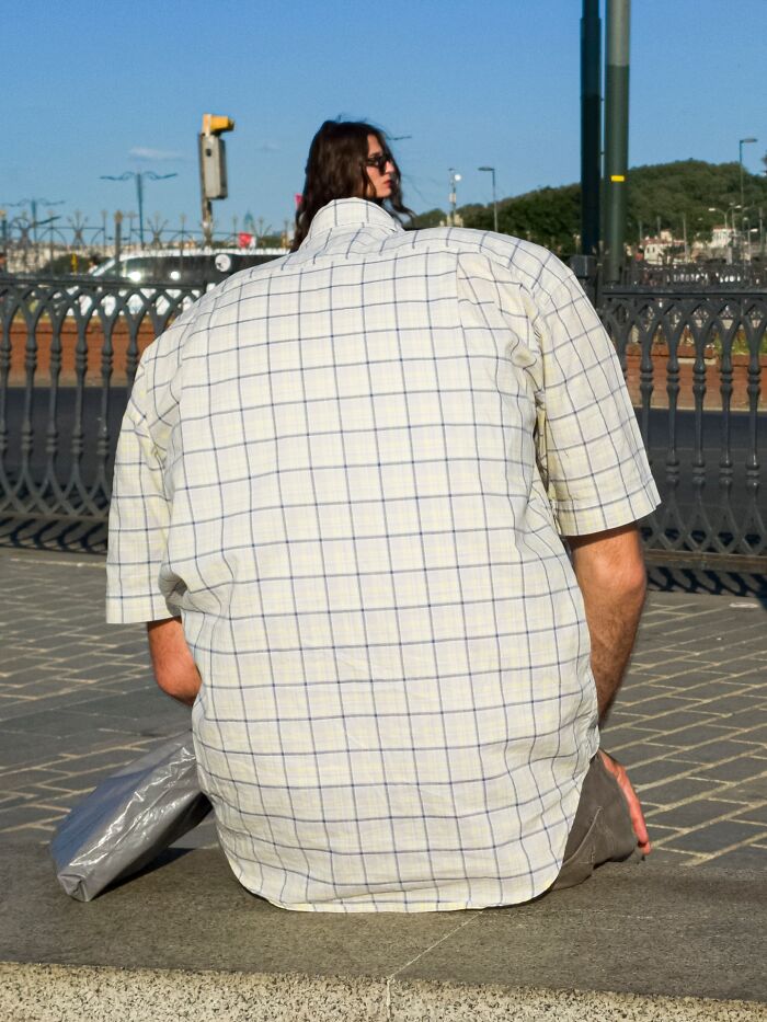 Man wearing a checkered shirt blending perfectly with a woman’s head creating a witty street coincidence outdoors.